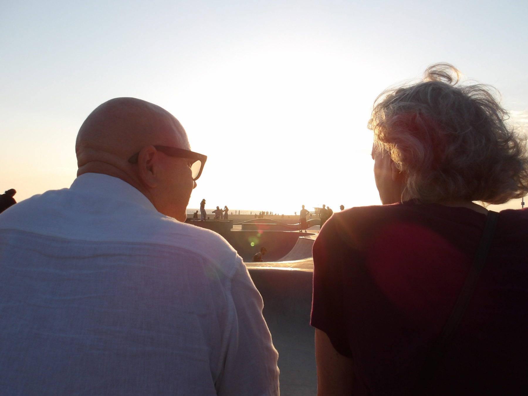 Two people watching a skatepark against the evening light