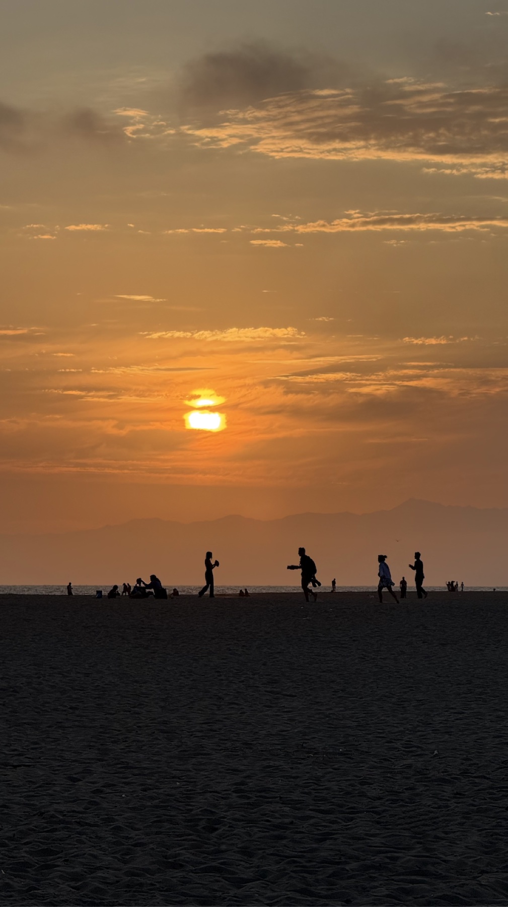 Silhouettes on the beach beneath an orange sunset